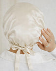 Person wearing a beige satin bonnet with a bow, Rosemary hair oil, pure silk hair bonnet, hairhalo, uk, haircare, healthy hair