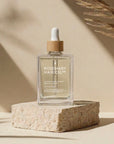 Rosemary Hair Oil Co. bottle on a stone platform with a neutral background. Rosemary hair oil, castor oil, camellia oil, apricot oil, hair growth, healthier, fuller-looking hair, stimulate, regrowth, hair thinning, natural, 100ml
