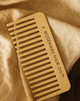 Wooden comb with 'Rosemary Hair Oil Co.' branding on a beige fabric background, Beige comb with 'Rosemary Hair Oil Co.' branding on a beige background, wide tooth flat comb,