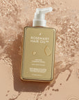 Rosemary Hair Oil Co. bottle on a textured beige background. Hair Rosé Hydrating Parfum Mist. Rosemary hair oil bottle with pump and pink roses on a beige background. “Luxury hair perfume mist designed to hydrate dry hair and add a soft floral scent.
