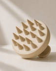 A round silicone scalp massager with multiple cone-shaped silicone spikes, shown on a warm beige background with soft diagonal shadows. Rosemary hair oil, scalp massager, soothe, essential, hair growth, stimulate, health, haircare, UK