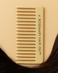 Beige comb with 'Rosemary Hair Oil Co.' branding on a beige background with hair. Beige comb with 'Rosemary Hair Oil Co.' branding on a beige background, wide tooth flat comb,