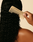 Person combing their hair with a wooden comb labeled 'Rosemary Hair Oil' against a beige background, Beige comb with 'Rosemary Hair Oil Co.' branding on a beige background, wide tooth flat comb,