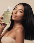 Woman holding a bottle of Rosemary Hair Oil with a beige background. Hair Rosé Hydrating Parfum Mist. Hydrating hair mist infused with rose water to refresh, soften and lightly fragrance hair