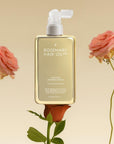 Hair Rosé Hydrating Parfum Mist. Rosemary hair oil bottle with pump and pink roses on a beige background. “Luxury hair perfume mist designed to hydrate dry hair and add a soft floral scent. 